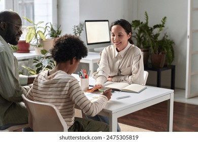 Portrait of smiling young woman as psychologist helping Black family in therapy session with young child drawing pictures - Powered by Shutterstock