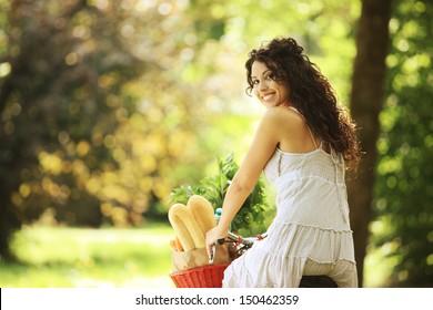 Portrait Of A Smiling Young Woman Riding Bicycle With Groceries In Basket