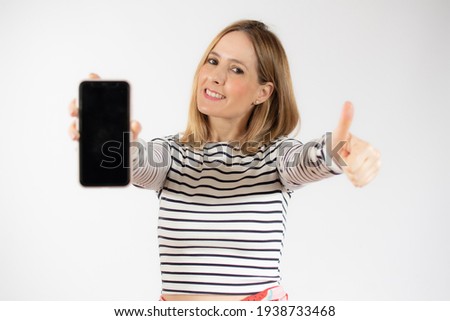 Portrait of a smiling young woman showing blank screen mobile phone while standing isolated over white background