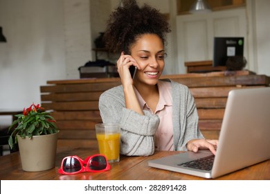 Portrait of a smiling young woman using laptop and talking on mobile phone