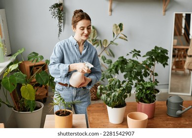 Portrait of smiling young woman watering plants indoors and caring for home greenery, copy space