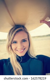 Portrait Of A Smiling Young Woman In Wet Suit Holding Surfboard Over Head At Beach