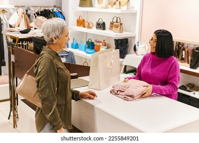 Portrait of smiling young woman working in clothing boutique and greeting senior customer