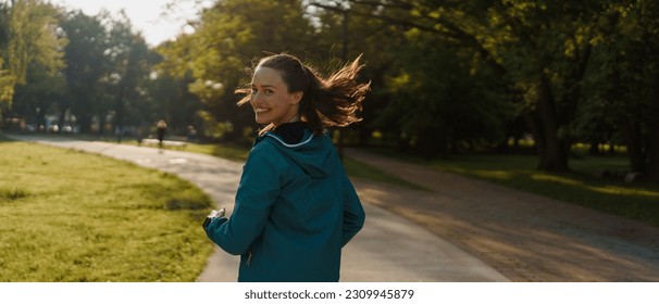 Portrait of smilling young woman running in the city park in the early morning. - Powered by Shutterstock