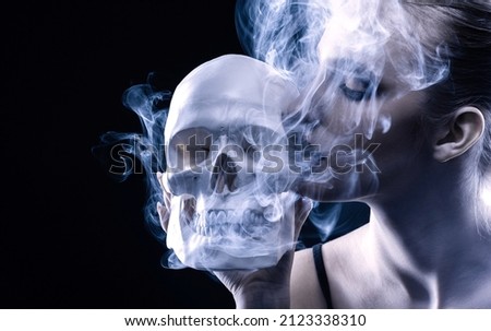 Portrait of a smoking girl with a skull in her hands on a dark background. smoking kills.