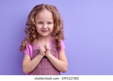 Portrait Of Sneaky Scheming Little Girl In Casual Wear Thinking Over Cunning Prank And Smirking, Disobedient Child Having Sly Tricky Plans In Mind. Indoor Studio Shot Isolated On Purple Background