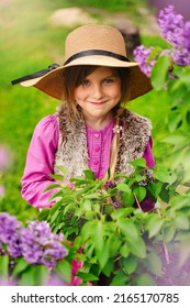 Portrait Of Sneaky Scheming Little Girl In Casual Wear Thinking Over Cunning Prank And Smirking, Disobedient Child Having Sly Tricky Plans In Mind. Outdoor Garden Shot Purple Background