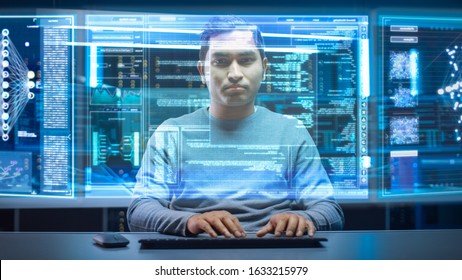 Portrait of Software Developer / Hacker Wearing Glasses Sitting at His Desk and Working on Futuristic Transparent Computer in Digital Identity Cyber Security Data Center. Hacking or Programming.