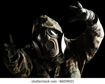 portrait of soldier with jungle camouflage and gas mask trying to hold something over black