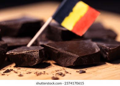 A portrait of some rough cut pieces of tasty delicious brown dark Belgian chocolate lying on a wooden surface, with a little blurred Belgian flag in between them.