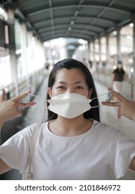 A portrait of a Southeast Asian female holding a medical mask in front of her face in the overground crossing
