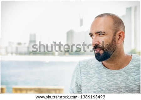 Portrait of a spanish man with beard and short buzz hair, looking away, casual, pensive, dreaming, profile view over urban background.