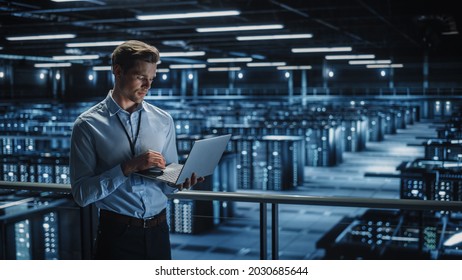 Portrait of IT Specialist Uses Laptop in Data Center. Server Farm Cloud Computing Facility with Male Maintenance Administrator Working. Cyber Security and Network Protection.