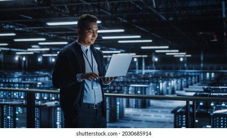Portrait of IT Specialist Uses Laptop in Data Center. Server Farm Cloud Computing Facility with Male System Administrator Working. Cyber Security and Network Protection.
