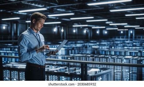 Portrait of IT Specialist Uses Laptop in Data Center. Server Farm Cloud Computing Facility with Male Maintenance Administrator Working. Cyber Security and Network Protection.
