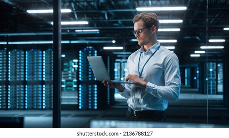 Portrait of IT Specialist Uses Laptop in Data Center. Server Farm Cloud Computing Facility with Male Maintenance Administrator Working. Cyber Security and Network Protection - Shutterstock ID 2136788127