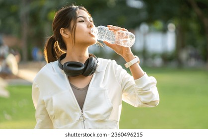 Portrait sport asian beauty body slim woman drinking water from a bottle while relax and feeling fresh,  refresh drink,  wellness, healthcare, mineral at green park.Healthy liquid lifestyle concept