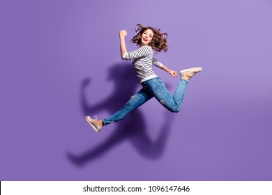 Portrait of sportive active girl in motion jumping over in the air isolated on violet background having perfect stretching looking at camera