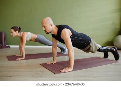 Portrait of sportive young couple working out indoors with man with prosthetic leg standing in plank - Powered by Shutterstock