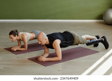 Portrait of sportive young couple working out indoors with man with disability doing planks - Powered by Shutterstock