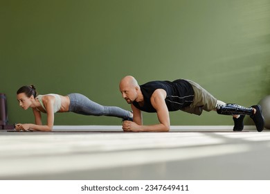 Portrait of sportive young couple working out indoors with man with prosthetic leg doing plank exercise - Powered by Shutterstock