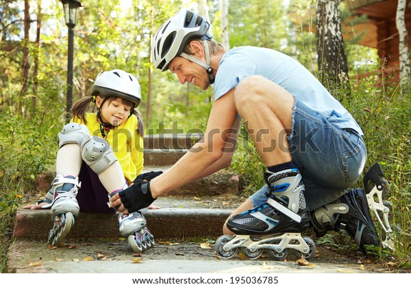 portrait of a sports dad and\
daughter in a helmet. Dad with his little daughter on the\
skates