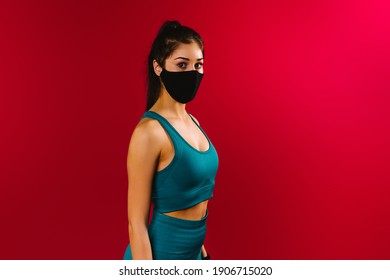 Portrait of a sports girl in a top and leggings on a red background with a protective black mask. The concept of training during quarantine. - Shutterstock ID 1906715020