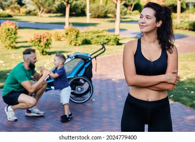 Portrait of a sports mom wearing sportswear over background of her husband and son after a workout and exercises in a city park. Happy sports family