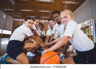 Portrait of sports teacher and school kids forming hand stack in basketball court at school gym - Powered by Shutterstock