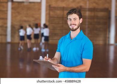 Portrait of sports teacher writing on clipboard in basketball court at school gym - Powered by Shutterstock