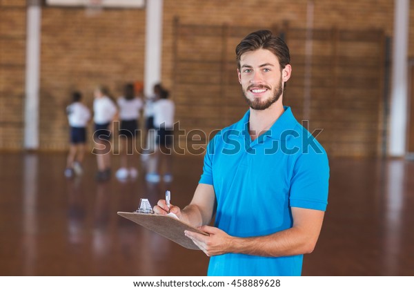 Portrait of sports teacher writing on\
clipboard in basketball court at school\
gym