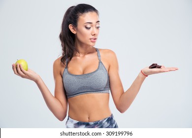 Portrait of a sports woman choosing between apple or chocolate isolated on a white background