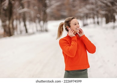 Portrait of sportswoman enjoying music while standing in nature on snowy weather. Winter fitness, healthy life, music, fun