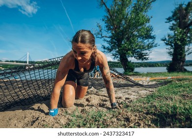 Portrait of a sportswoman participating in an physically demanding obstacle course race while crawling under the net and overcoming one of the obstacles. OCR race concept. Copy space. - Powered by Shutterstock