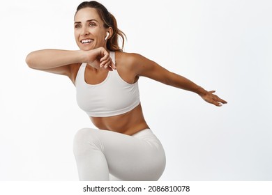 Portrait of sportswoman stretching body, exercising, doing fitness leg raise and smiling, running, standing over white background - Shutterstock ID 2086810078