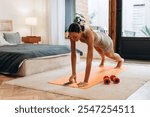 Portrait of sporty African American woman turning on the timer on smartphone, doing plank exercise at home. Healthy lifestyle, sport concept