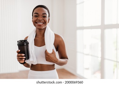 Portrait of sporty beautiful smiling black woman in white sportswear and towel on neck holding shaker with healthy drink, whey protein, fresh water or coffee isolated, posing looking at camera - Powered by Shutterstock