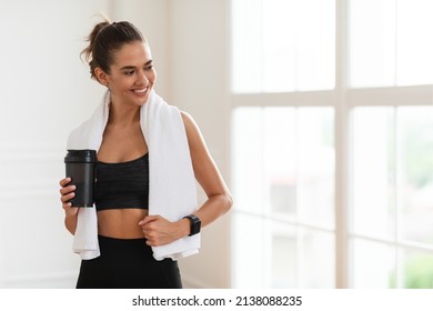 Portrait of sporty beautiful smiling lady in sportswear and white towel on neck holding shaker with healthy drink, whey protein, fresh water or coffee and looking away at free copy space banner mockup