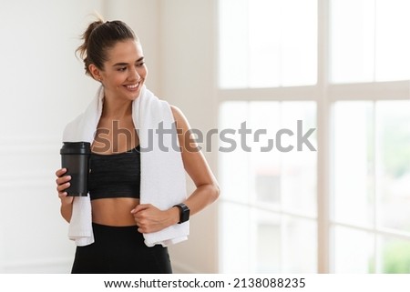 Portrait of sporty beautiful smiling lady in sportswear and white towel on neck holding shaker with healthy drink, whey protein, fresh water or coffee and looking away at free copy space banner mockup