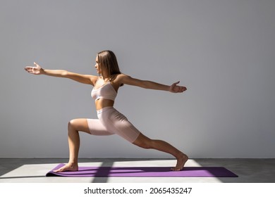 Portrait of sporty fit beautiful young brunette woman in sportswear bra and black pants working out, doing Utthita Trikonasana, Extended Triangle pose, studio full length, isolated, white background