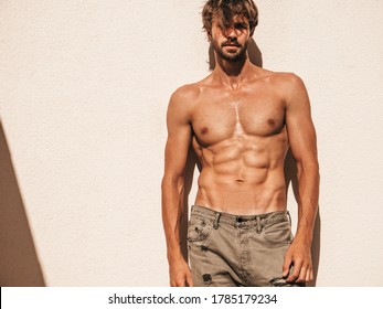 Portrait of sporty handsome strong man. Healthy athletic fitness model posing near white wall in jeans. Confident sexy fashion male with naked nude torso. Lambersexual outdoors
