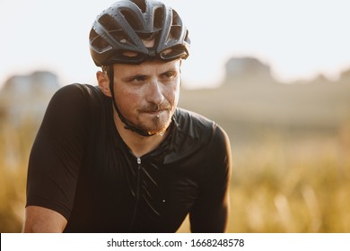 Portrait of sporty man in black helmet and cycling clothes being wet because of hard training and riding long distance. Professional bicyclist relaxing and gaining strength with blur background behind