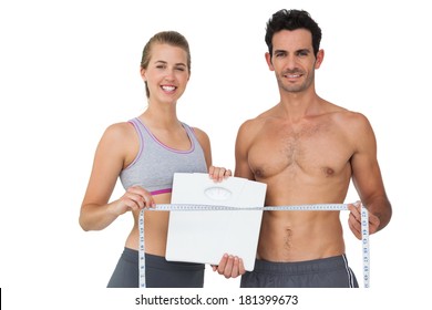 Portrait of a sporty young couple holding scales and measuring tape over white background