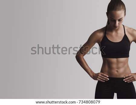 Portrait of sporty young woman with muscular body, posing against a gray background