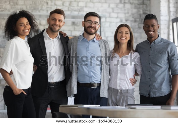 Portrait of\
standing in row smiling multiracial team embracing looking at\
camera. Happy diverse corporate staff, hugging specialists, bank\
workers photo shoot, HR agency\
recruitments.