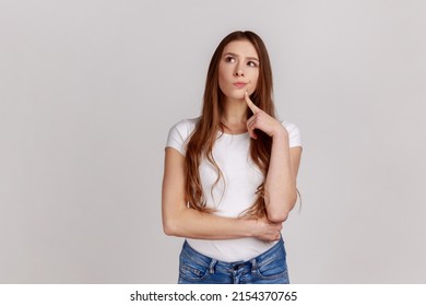 Portrait of standing with thoughtful serious smart expression, pondering answer, having doubts and suspicion, wearing white T-shirt. Indoor studio shot isolated on gray background.