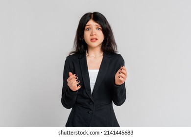 Portrait Of Startled Brunette Teen Girl Raising Hands And Gasping Worried, Staring Shocked And Confused At Camera, Standing In Black Blazer Over Grey Background