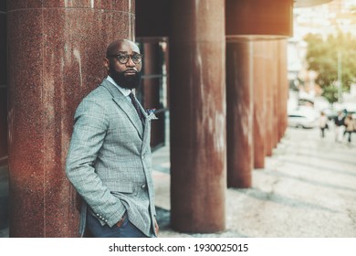 Portrait of a stately dapper man entrepreneur in eyeglasses and fashionable custom-made suit standing near the marble column of a building, with a copy space place on the right for an ad text message