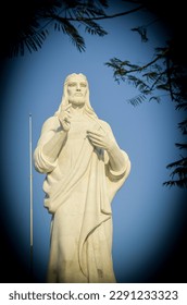 A portrait statue of the Sacred Heart of Jesus in close-up, set against a bright blue sky.