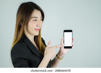 Portrait of stressed asian business woman showing and pointing to empty white mobile screen. Caucasian female model isolated on white background. selective focus